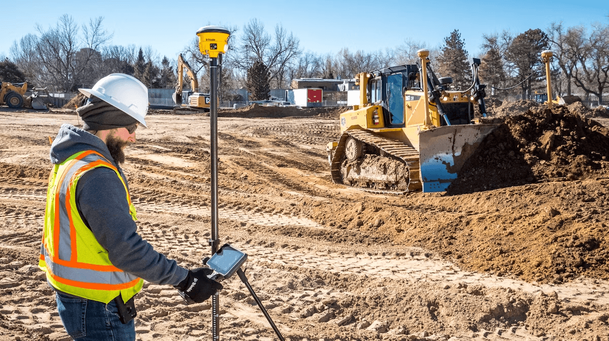 Surveyor using Trimble GPS rover on an active construction grading site